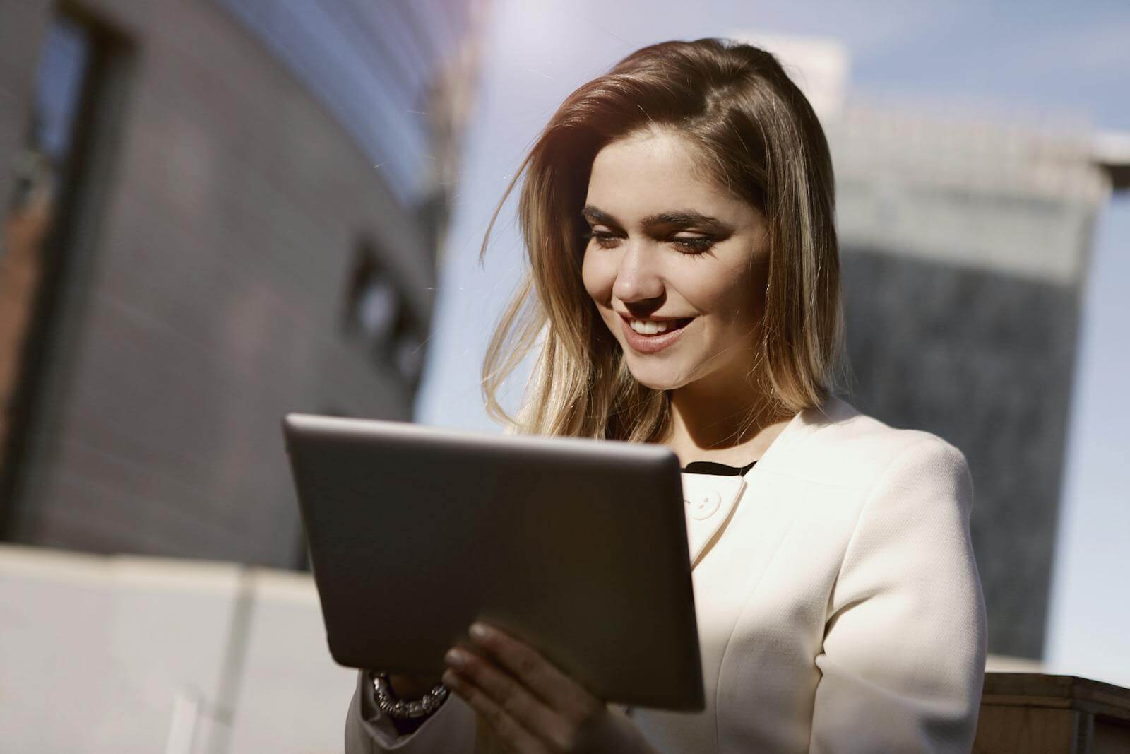 A woman joyfully using a digital tablet outdoors in the city during the day.